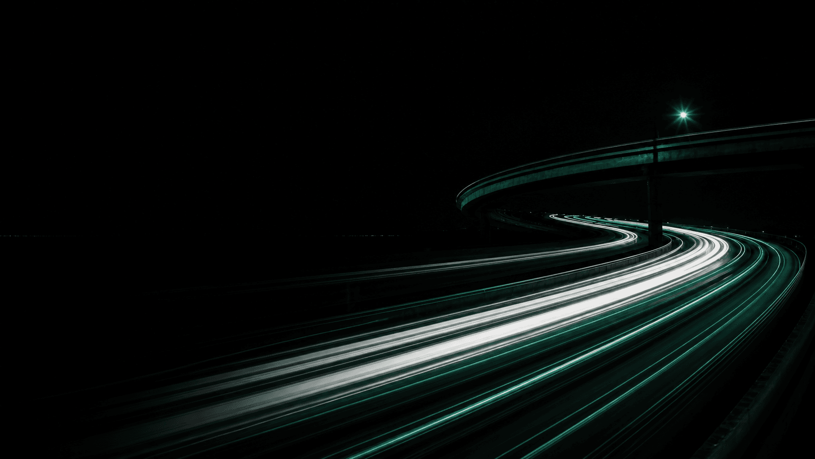 Emerald and white light trails curving through a dark elevated roadway